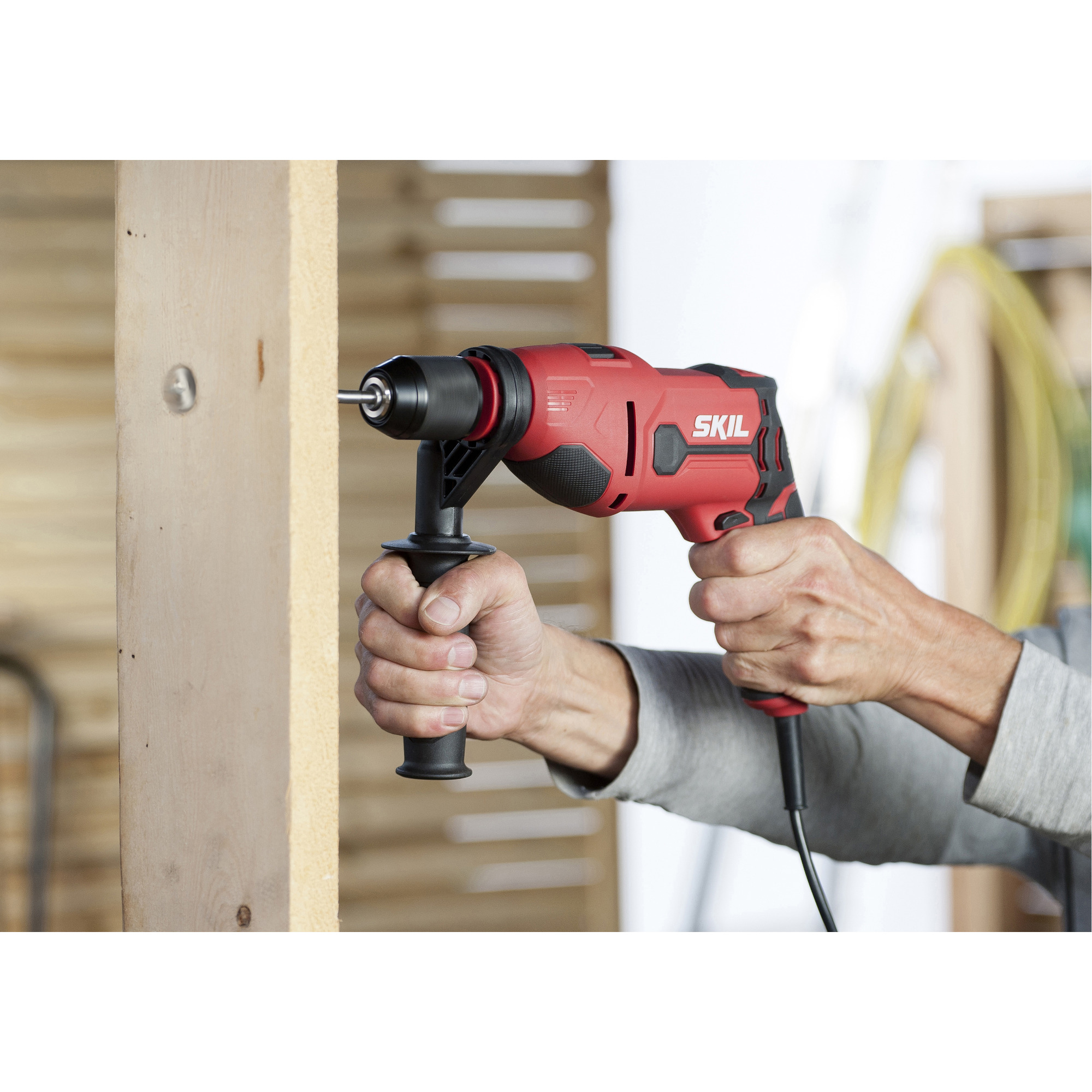 Persona che fora una tavola di legno con un trapano rosso Skil.