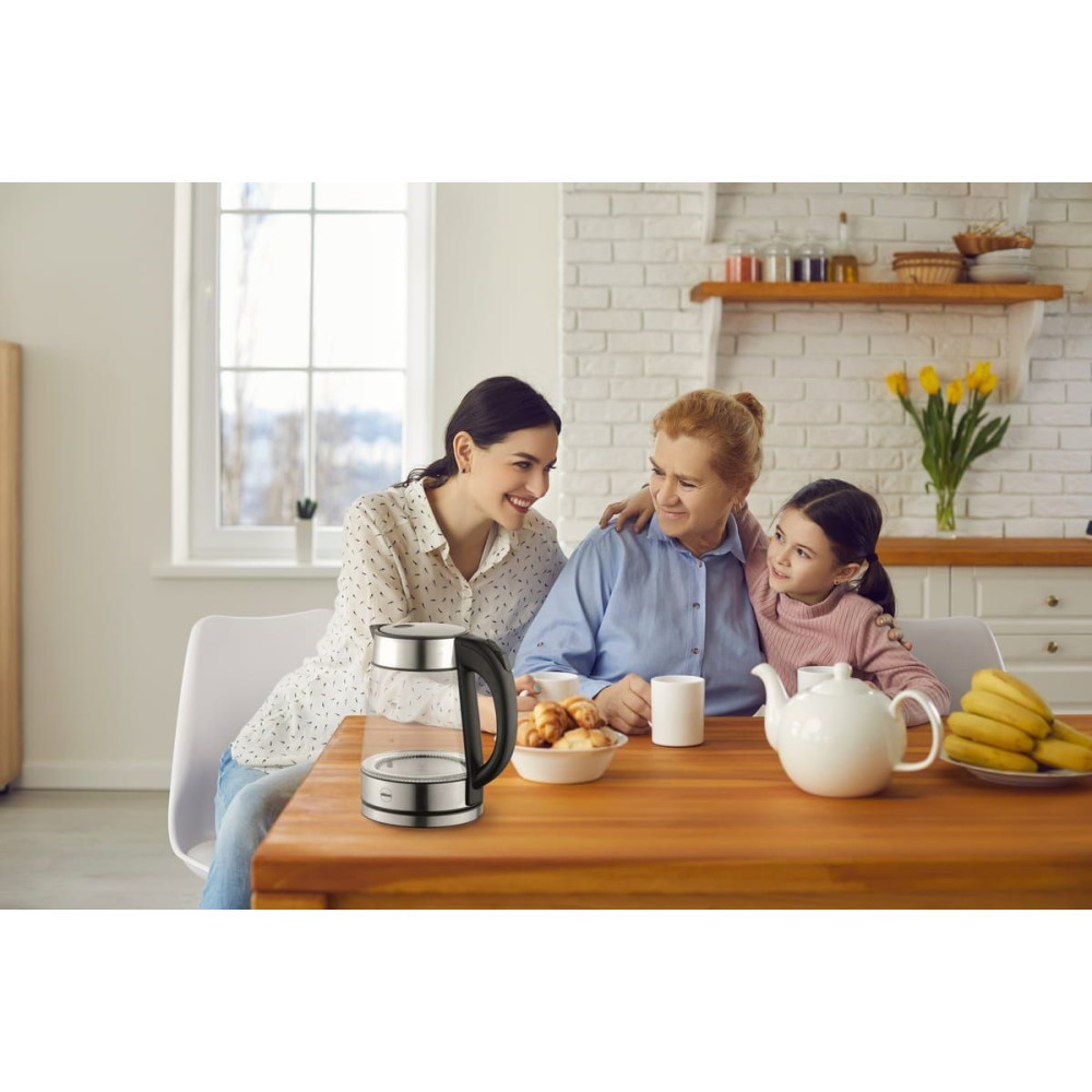 Trzy pokolenia kobiet uśmiechają się przy stole kuchennym ze szklanym czajnikiem.