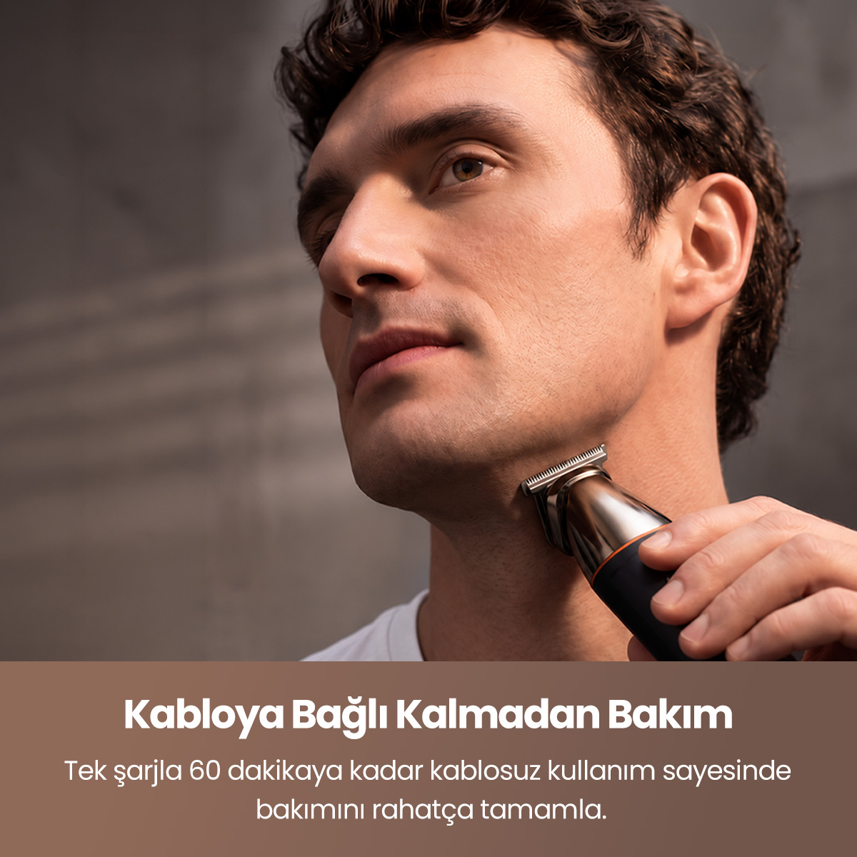 Koyu gri arka plan önünde elektrikli tıraş makinesiyle sakalını düzelten bir adam.