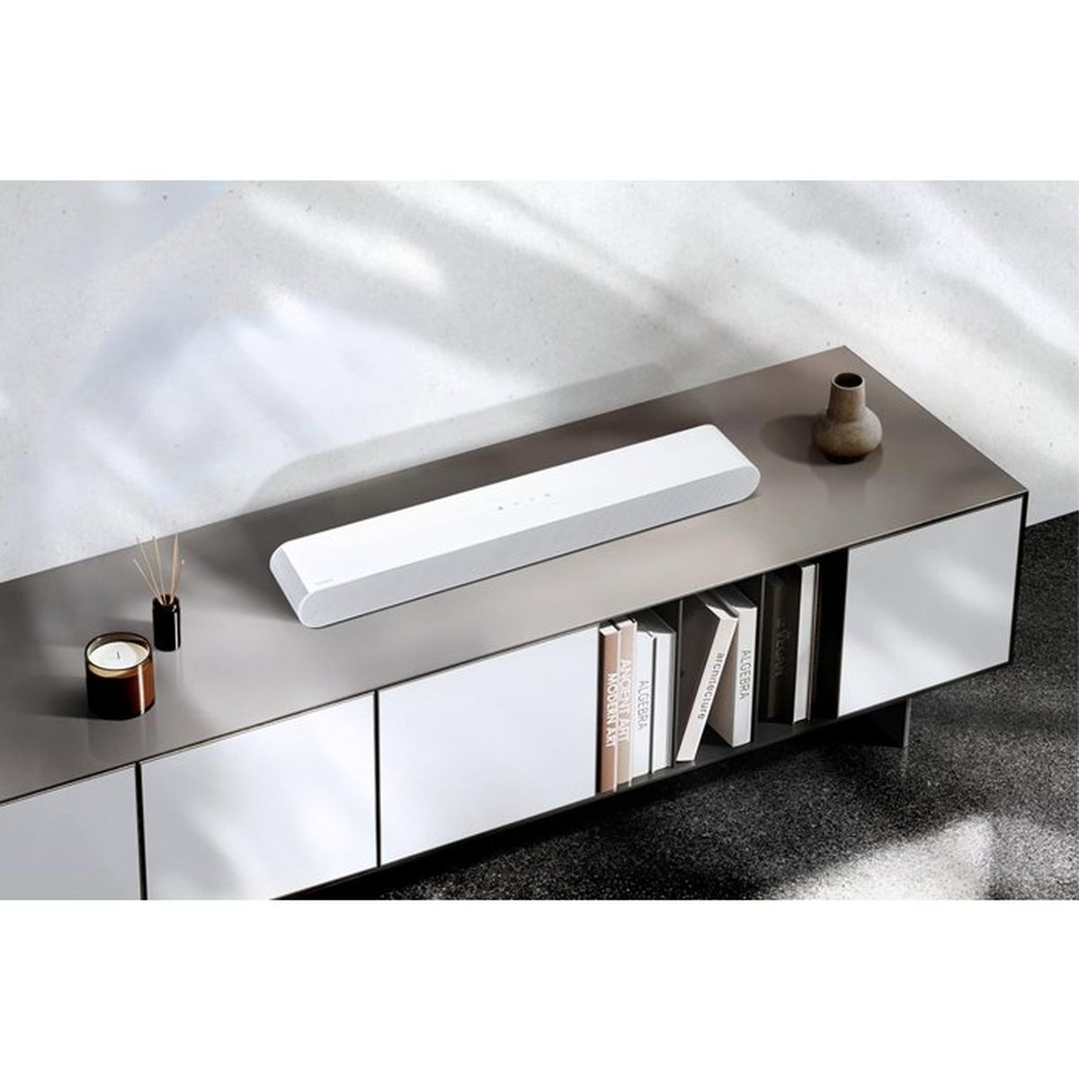 Una soundbar bianca si trova su un mobile moderno con libri sugli scaffali sottostanti.