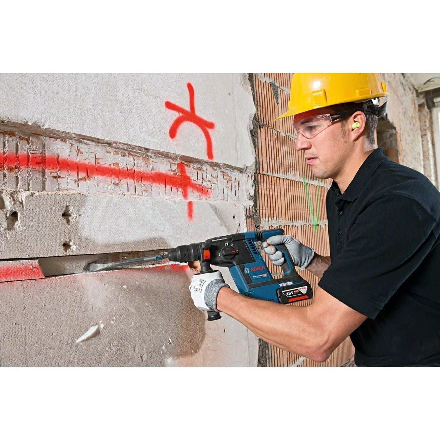 Ein Arbeiter mit Helm und Schutzbrille bohrt eine Wand in einem Raum mit einem Akku-Bohrhammer auf.