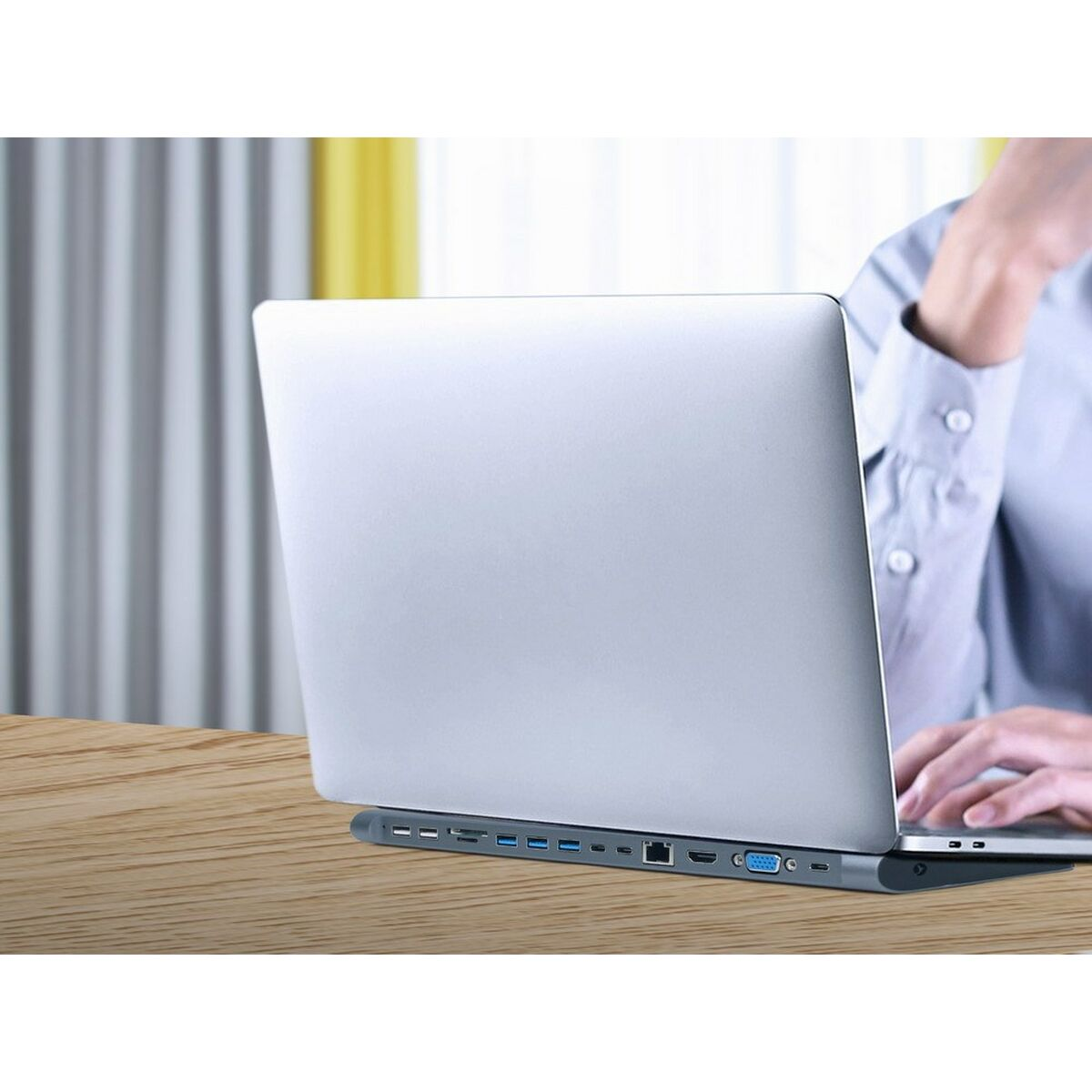 Eine Person tippt auf einem silbernen Laptop auf einem Docking-Station-Ständer auf einem Schreibtisch.