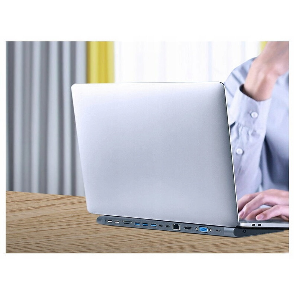 Ein Laptop steht auf einem Holztisch, verbunden mit einer grauen Dockingstation voller Ports.