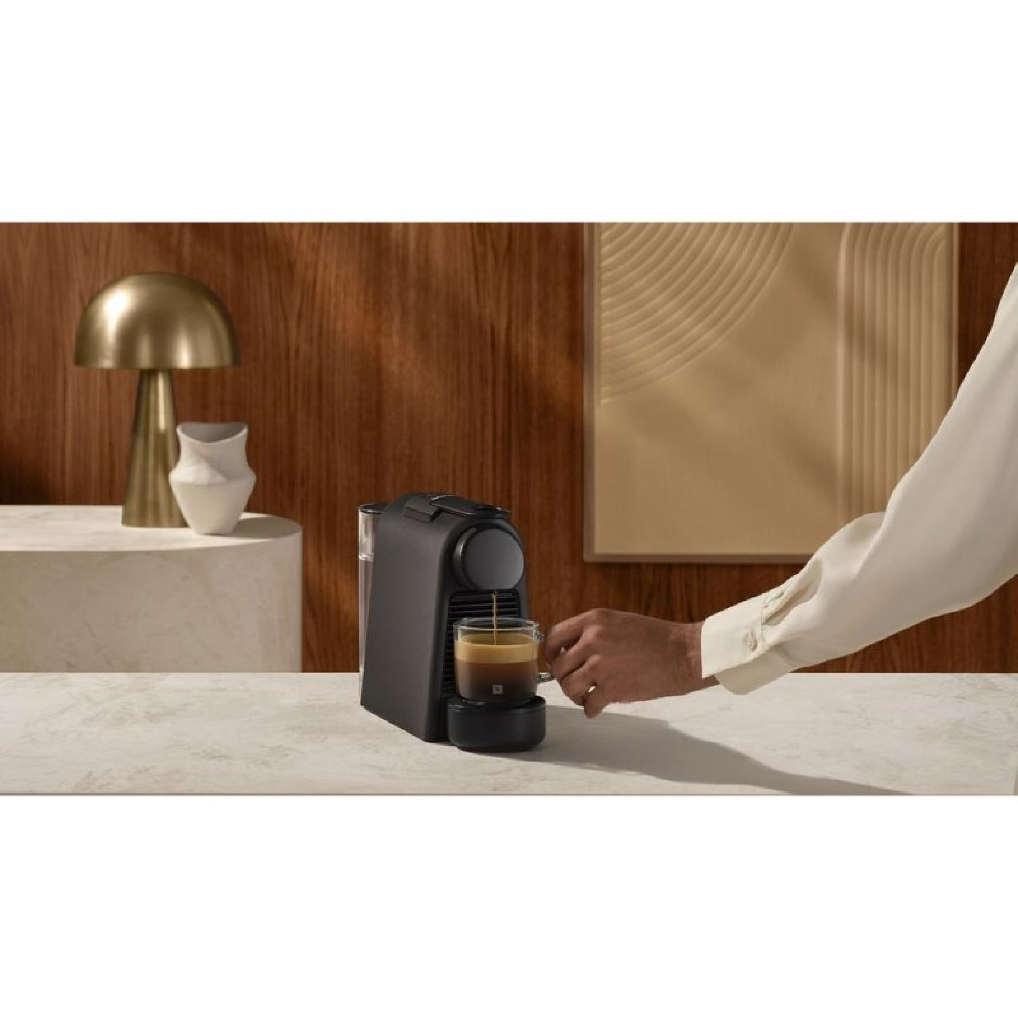 Eine Person gießt Kaffee aus einer schwarzen Maschine in eine Tasse auf einer Marmortheke.