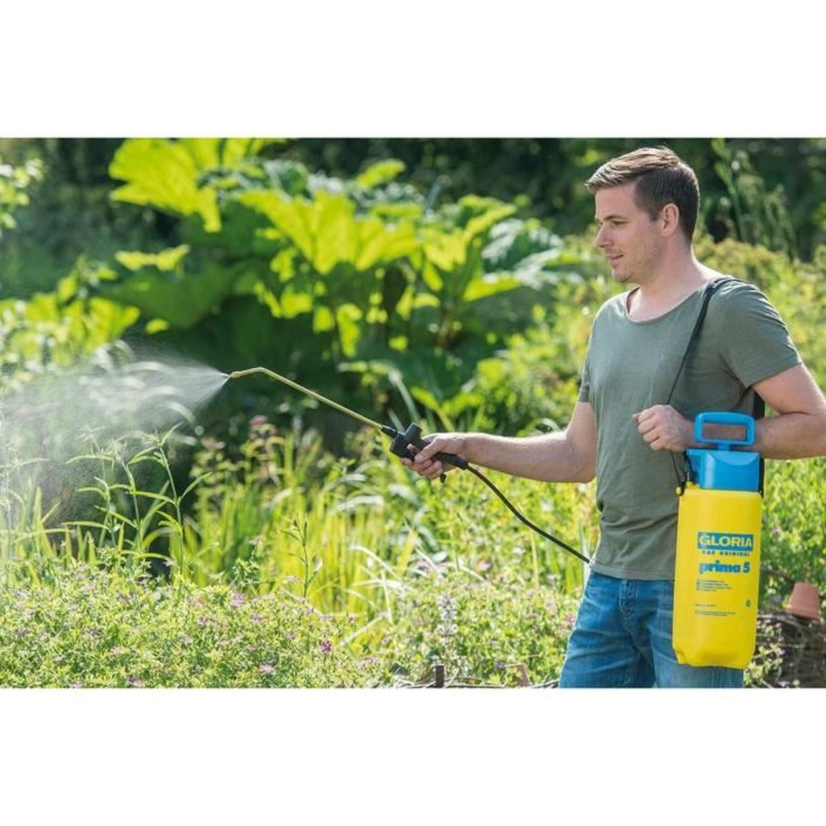 Ein Mann sprüht mit einem gelben Gloria-Pflanzensprüher Wasser auf grüne Gartenpflanzen.