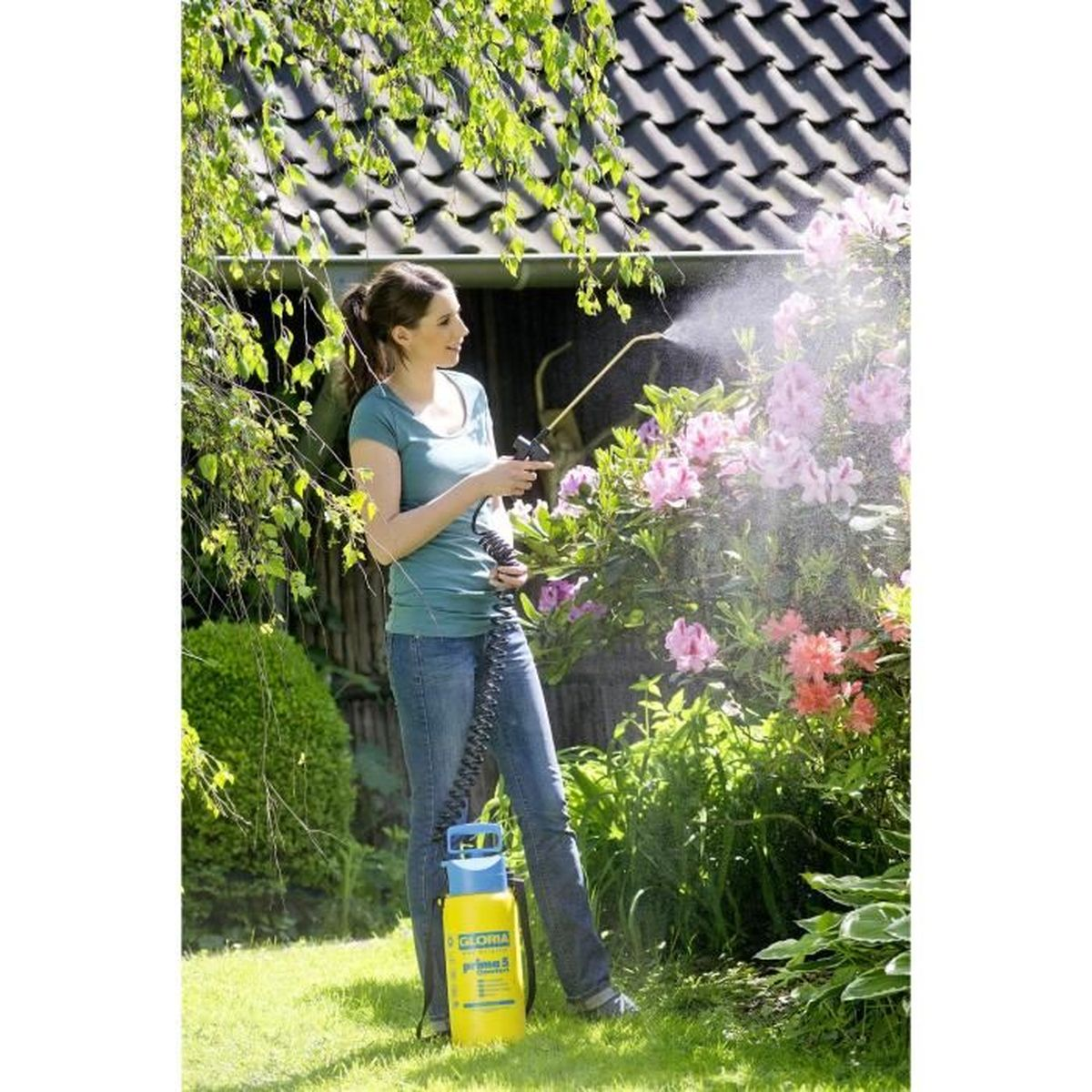 Eine Frau besprüht im Garten mit einem gelben Sprühgerät blühende Sträucher.