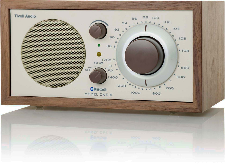 Ein hölzernes Tivoli Audio Model One BT Radio mit Lautsprecher, Reglern und Skala auf spiegelnder Oberfläche.