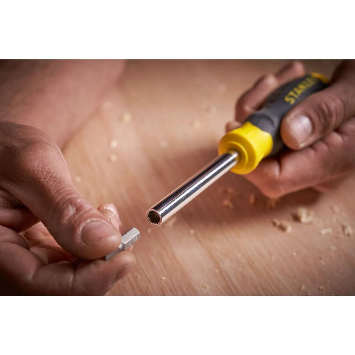 Eine Hand hält einen gelb-schwarzen Schraubenzieher, während die andere Hand einen kleinen Bit darüber hält.