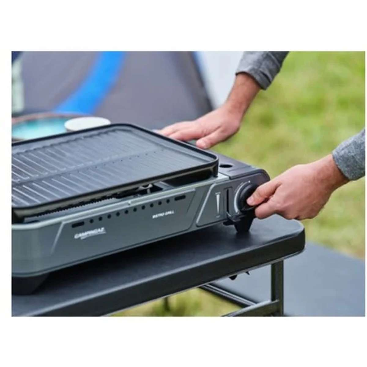 Una persona gira la manopola di controllo su un grill da campeggio grigio su un tavolo nero.