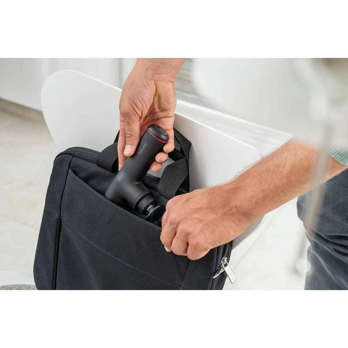 Una persona ripone una pistola da massaggio nera in una borsa nera per laptop.
