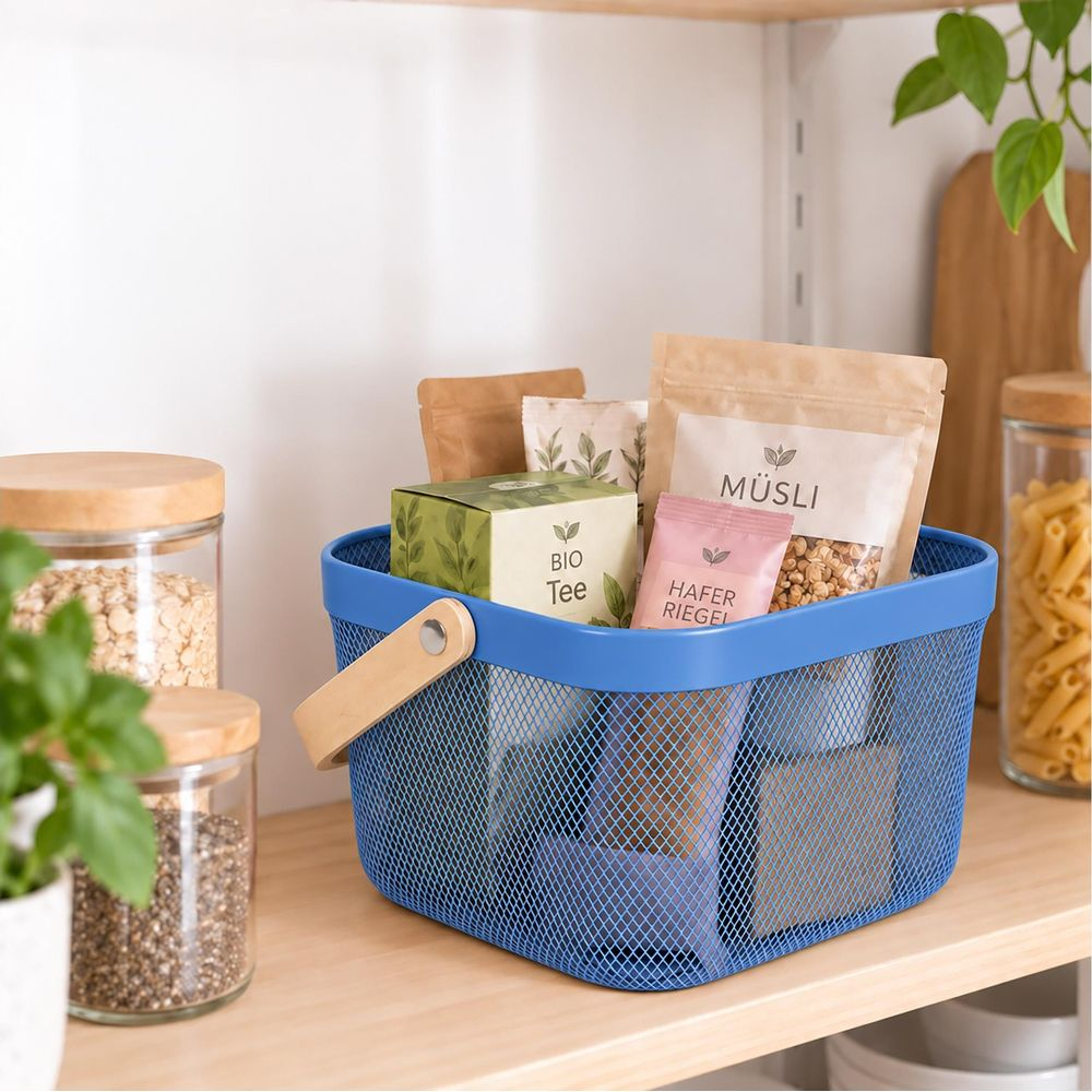 Ein blauer Metallkorb mit Holzgriffen steht auf einem Holzregal und enthält Tee, Müsli und Haferriegel.