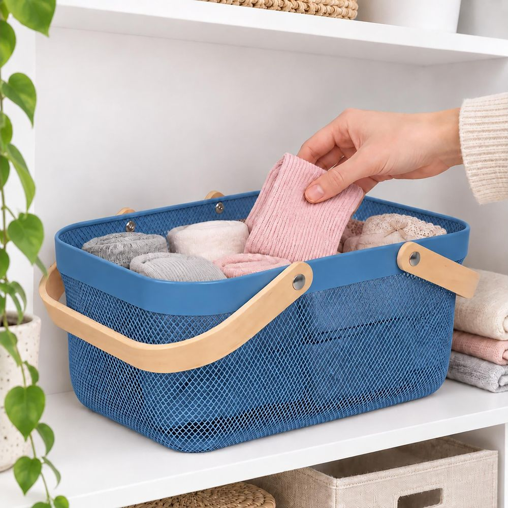 Eine Hand legt ein rosa Kleidungsstück in einen blauen Drahtkorb mit Holzgriffen auf einem Regal.