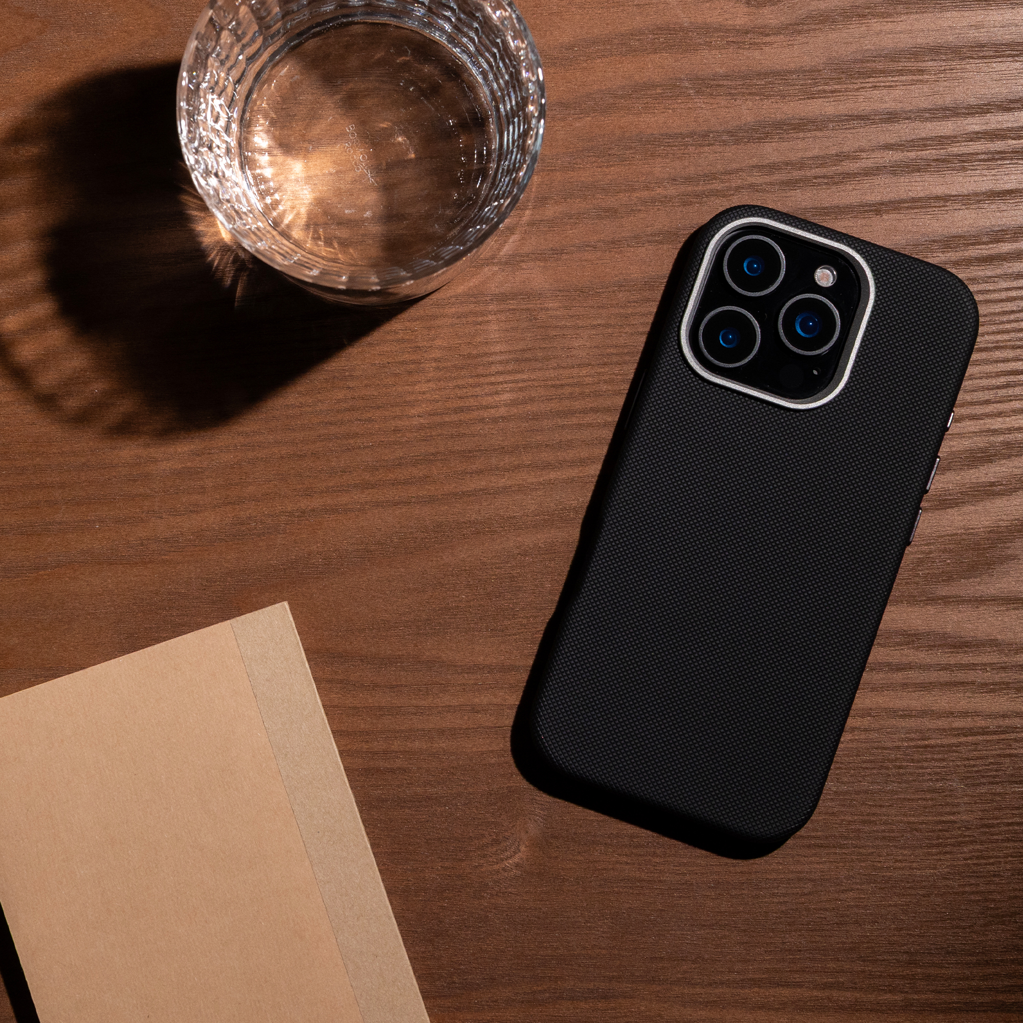 Un smartphone dans une coque, un verre d'eau et un carnet brun reposent sur une surface en bois.