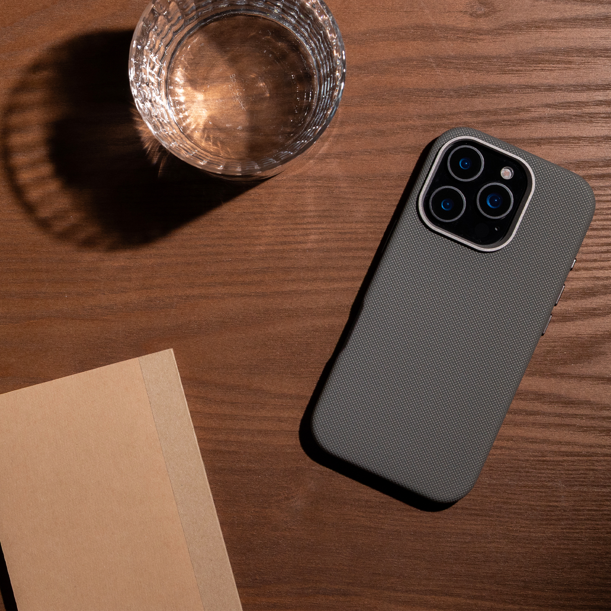 Un smartphone, un verre d'eau et un carnet sur une table en bois.
