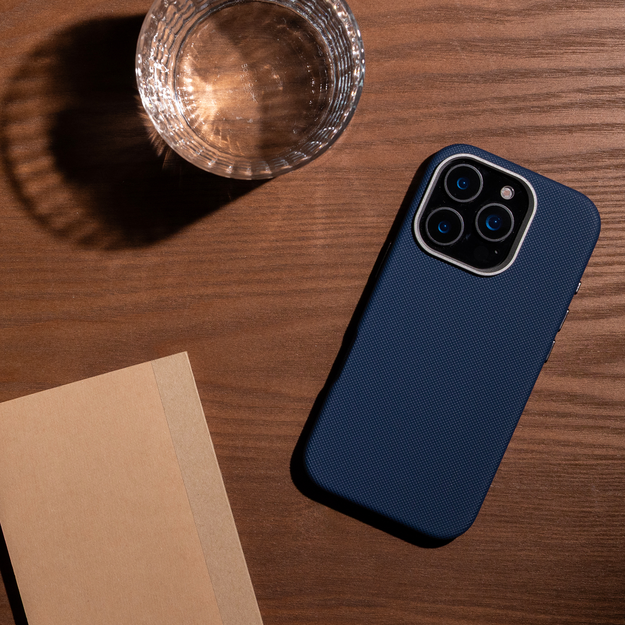 Un smartphone bleu foncé, un verre d'eau et un carnet reposent sur une surface en bois.