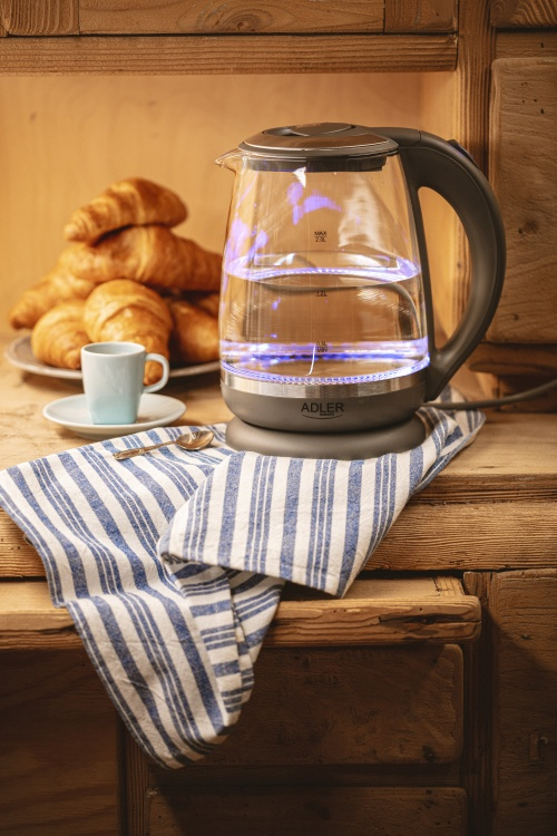 Ein leuchtender Glaskocher, Croissants und eine Tasse Kaffee stehen auf einem Holztisch mit blauem Handtuch.