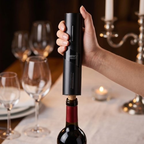 Una mano usa un apribottiglie elettrico nero su una bottiglia di vino a tavola.