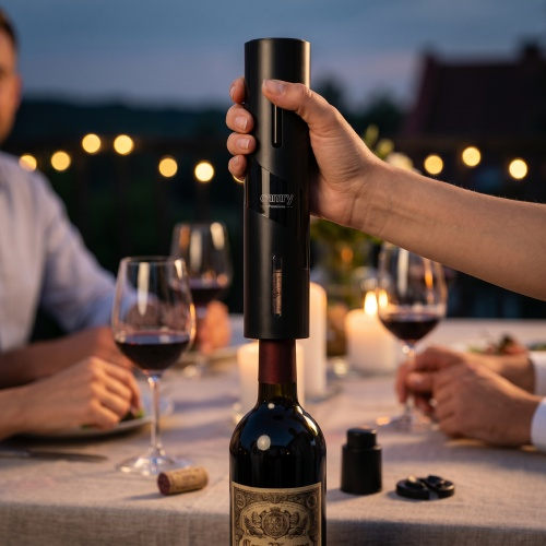 Una persona usa un apribottiglie elettrico su un tavolo con bicchieri di vino e candele.
