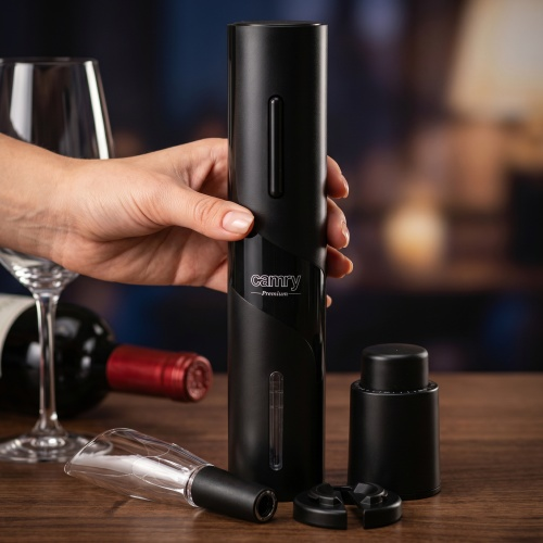 Mano tiene un apribottiglie elettrico nero su tavolo di legno accanto a calice.