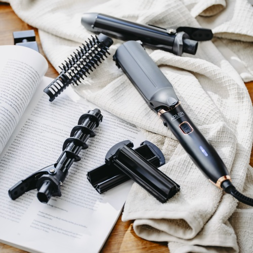 Un multi-styler nero con accessori su un asciugamano bianco e una rivista.