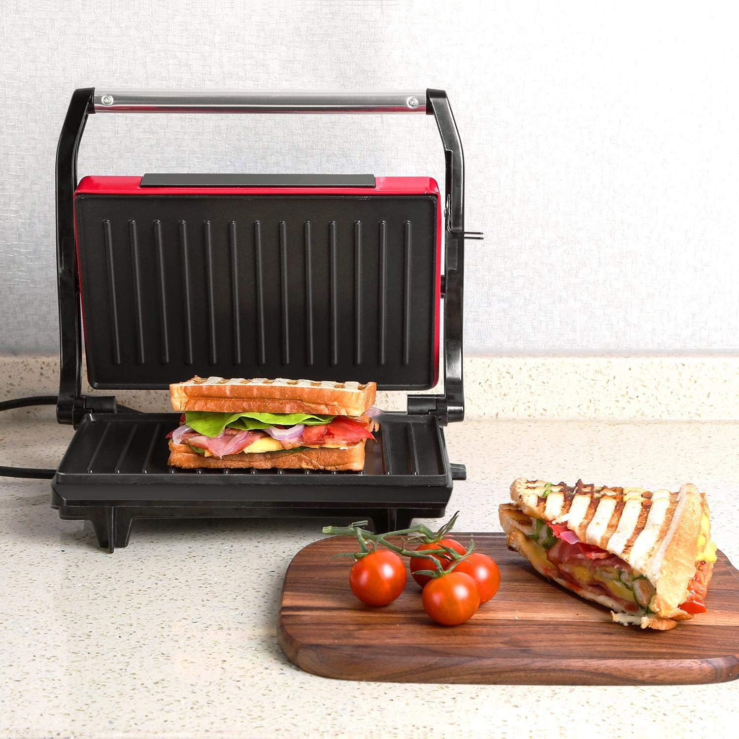 Griglia per sandwich con sandwich. Mezzo sandwich e pomodori su tagliere.