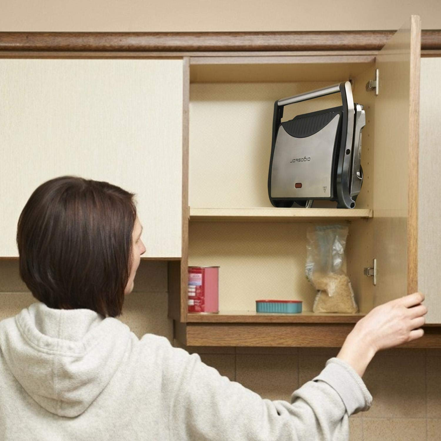 Una donna apre la porta di un armadio. All'interno c'è una sandwichera pieghevole argento e nera.