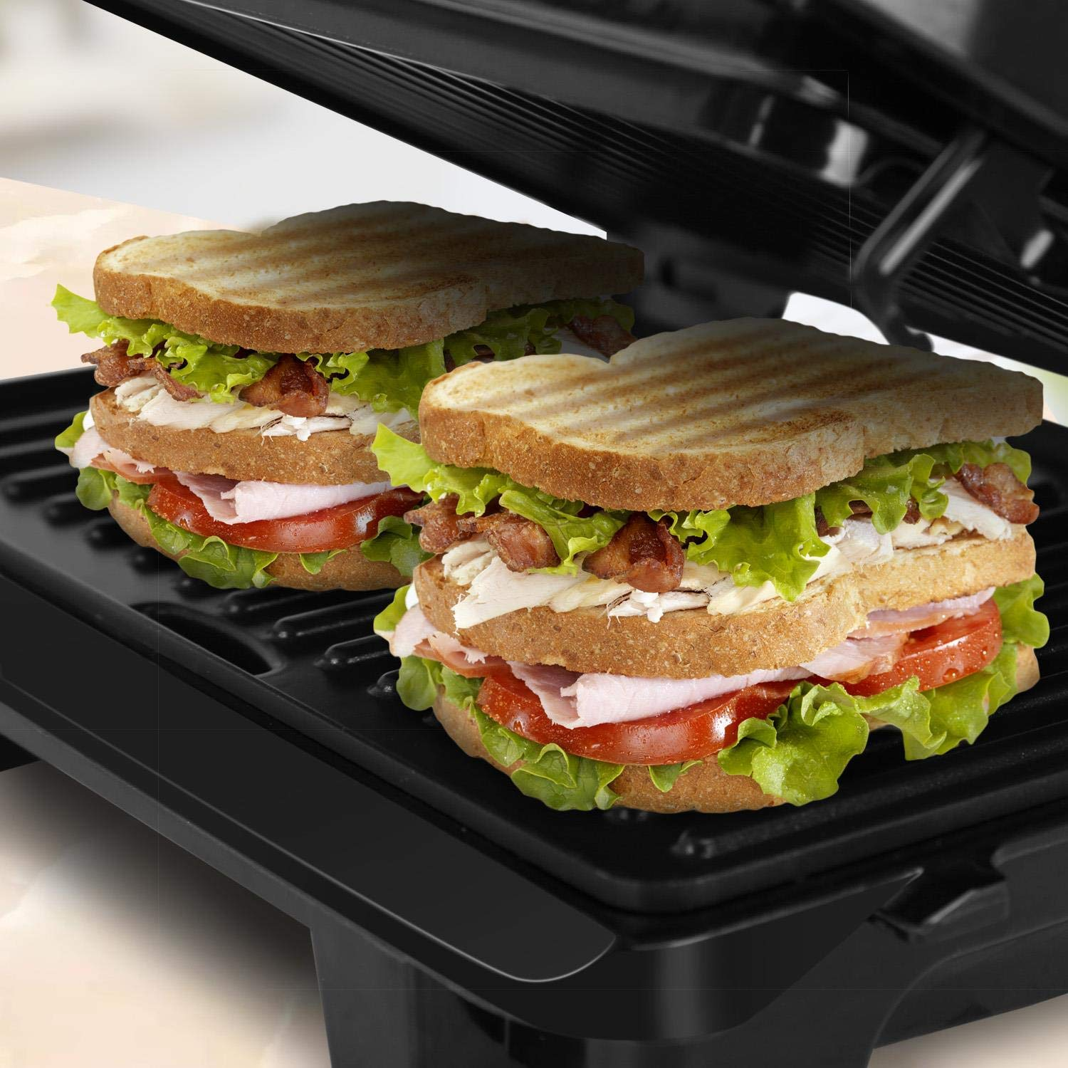 Due panini impilati su una griglia nera. Hanno lattuga, pomodoro, pancetta e pane.