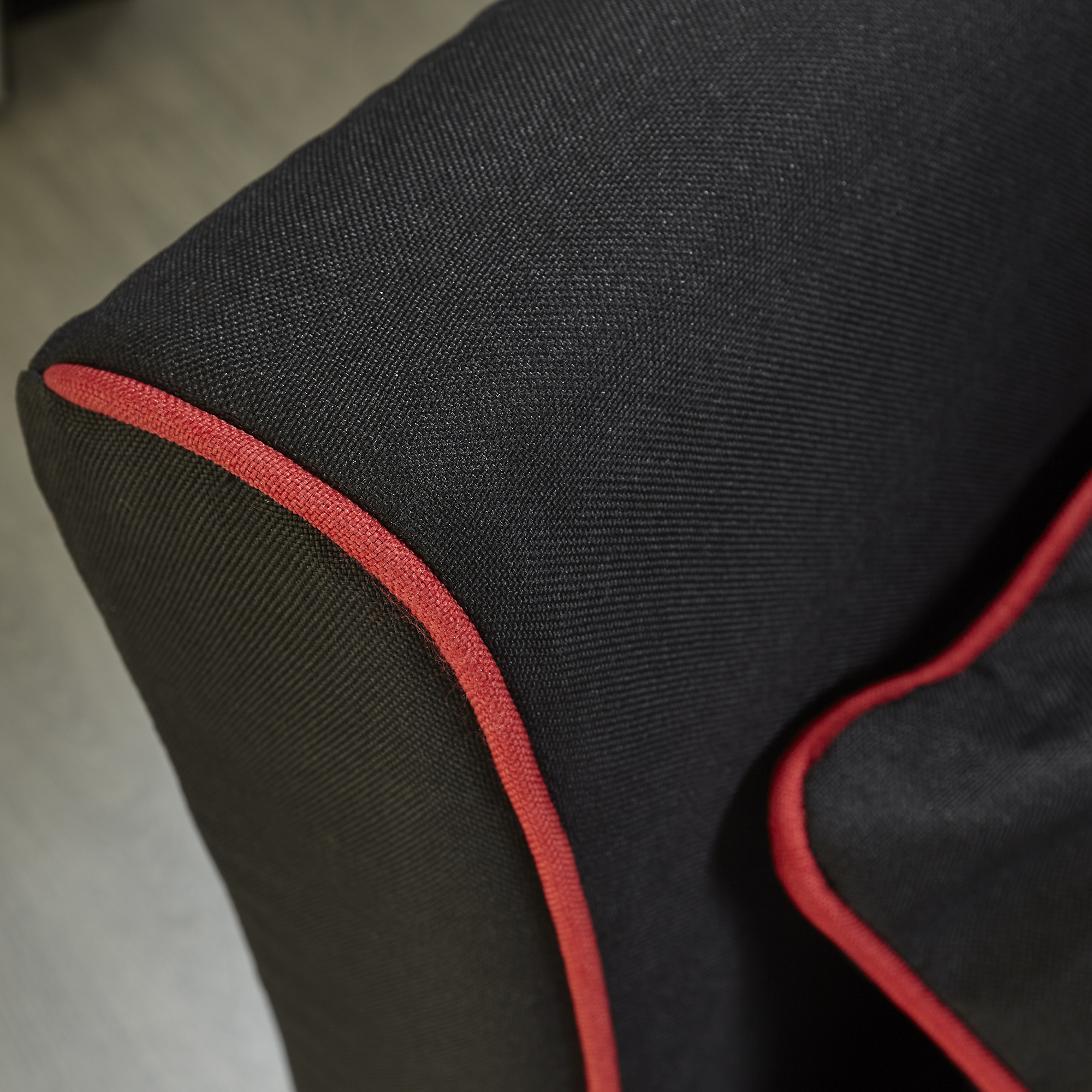 Nahaufnahme eines schwarzen Stoffstuhls mit roter Einfassung. Der Stuhl steht auf einer hellgrauen Oberfläche.