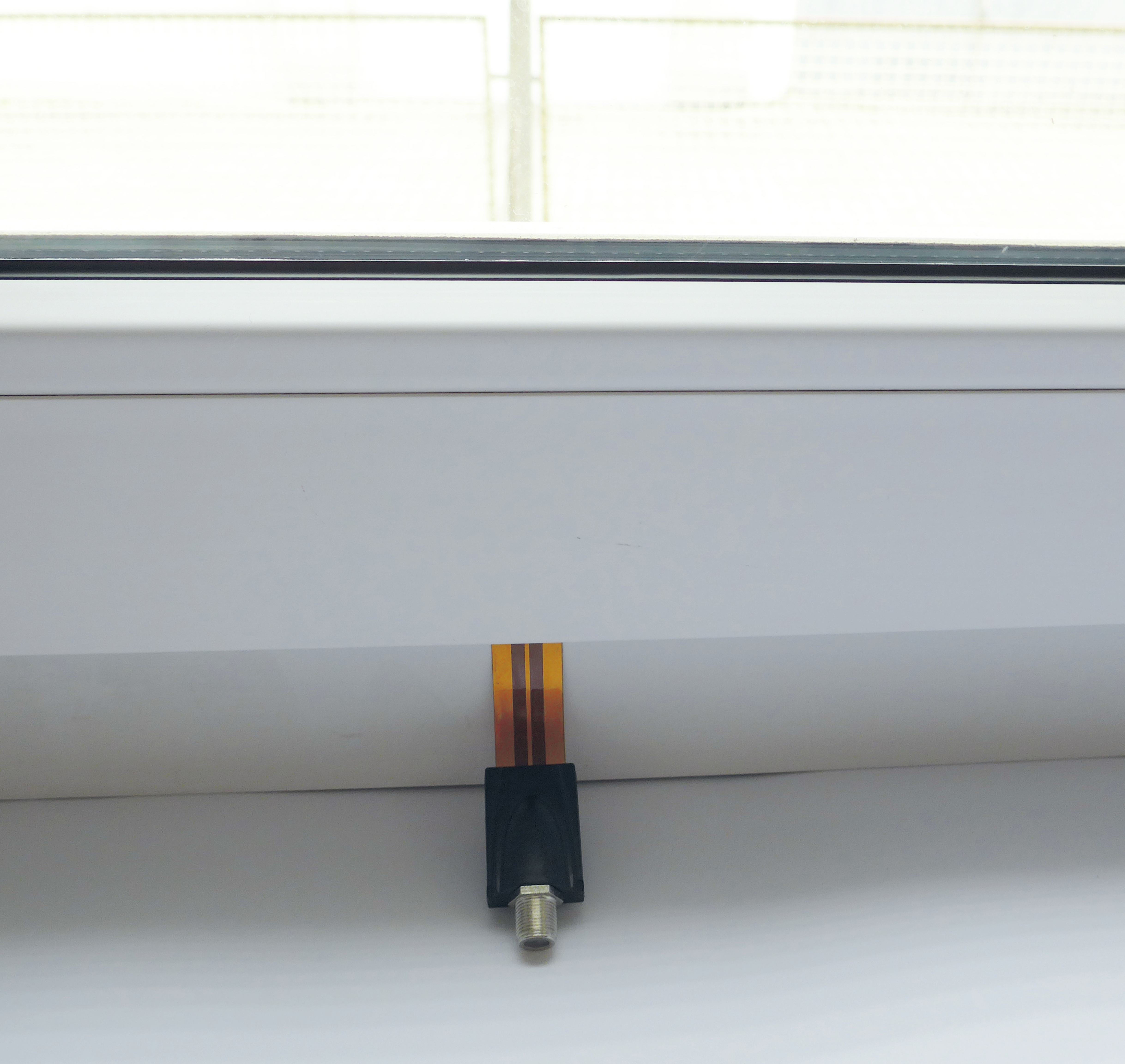 Ein kleiner schwarzer Stecker mit Kabel ist am Fensterrahmen befestigt. Das Fenster ist weiß.