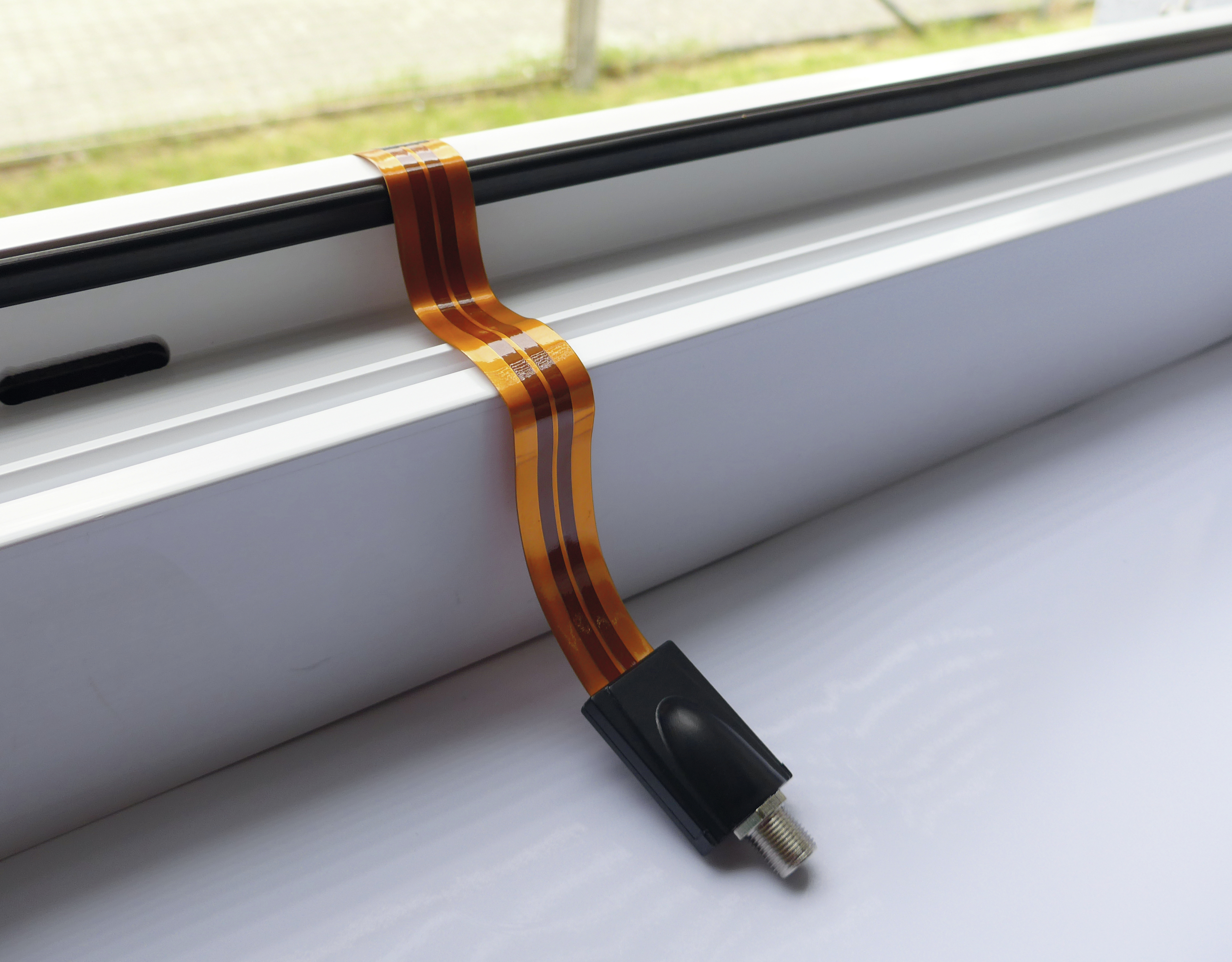 Ein dünnes, flexibles orangefarbenes Kabel mit schwarzem Stecker, auf weißer Oberfläche.