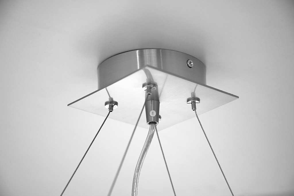 Deckenleuchte mit quadratischer Metallbasis, Kabeln und einem abgehängten Leuchtelement. Weißer Hintergrund.