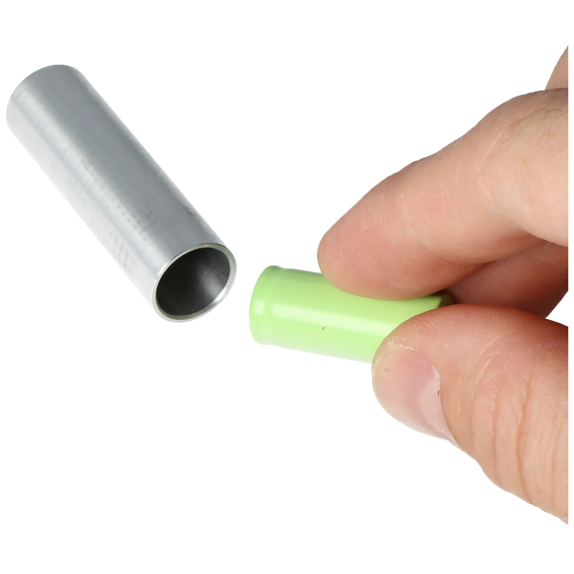 Die Hand einer Person hält eine grüne Batterie neben einem leeren Metallrohr.