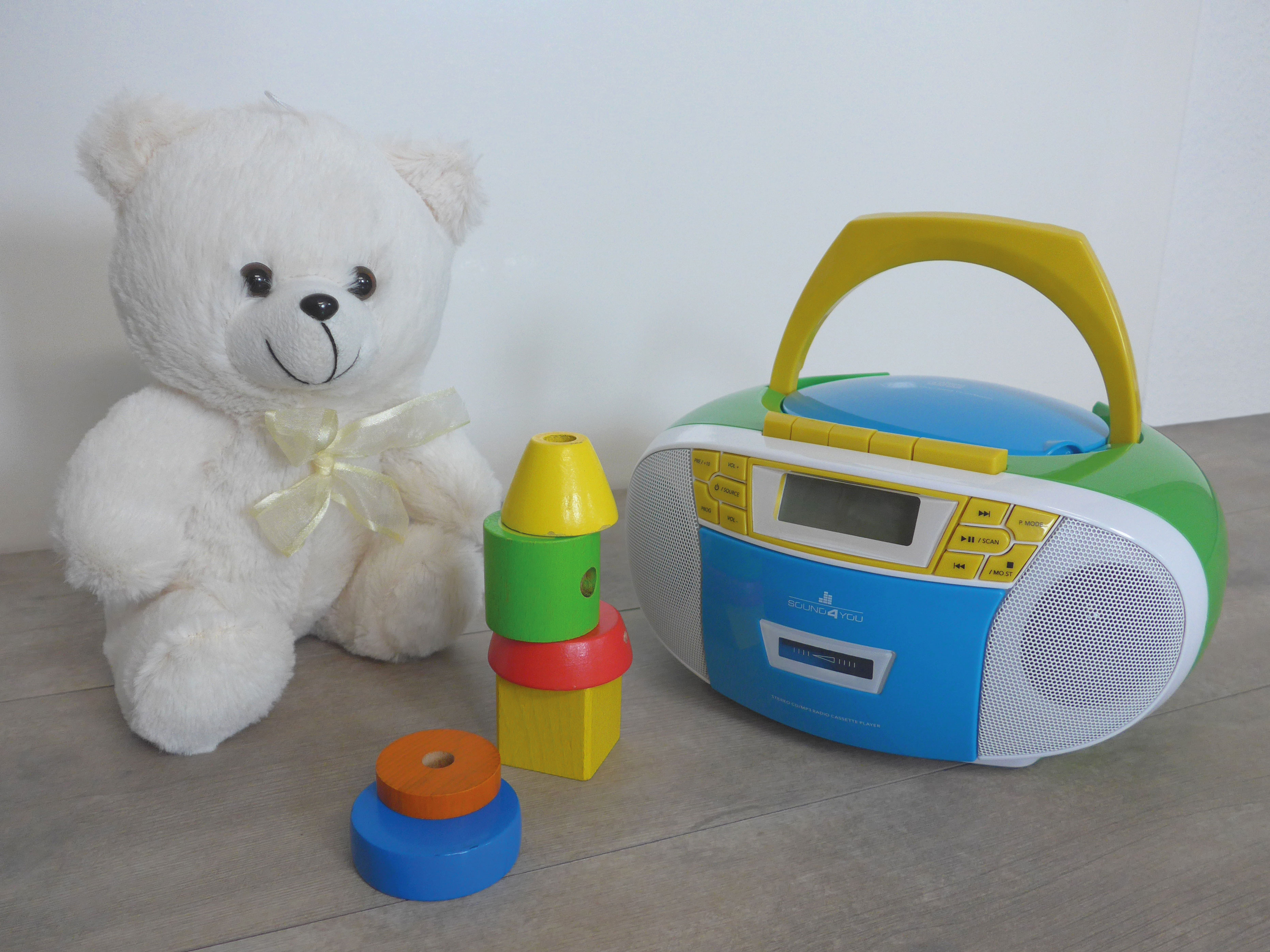 Ein Teddybär, Holzblöcke und eine blaue und grüne Boombox auf einem Holzboden.