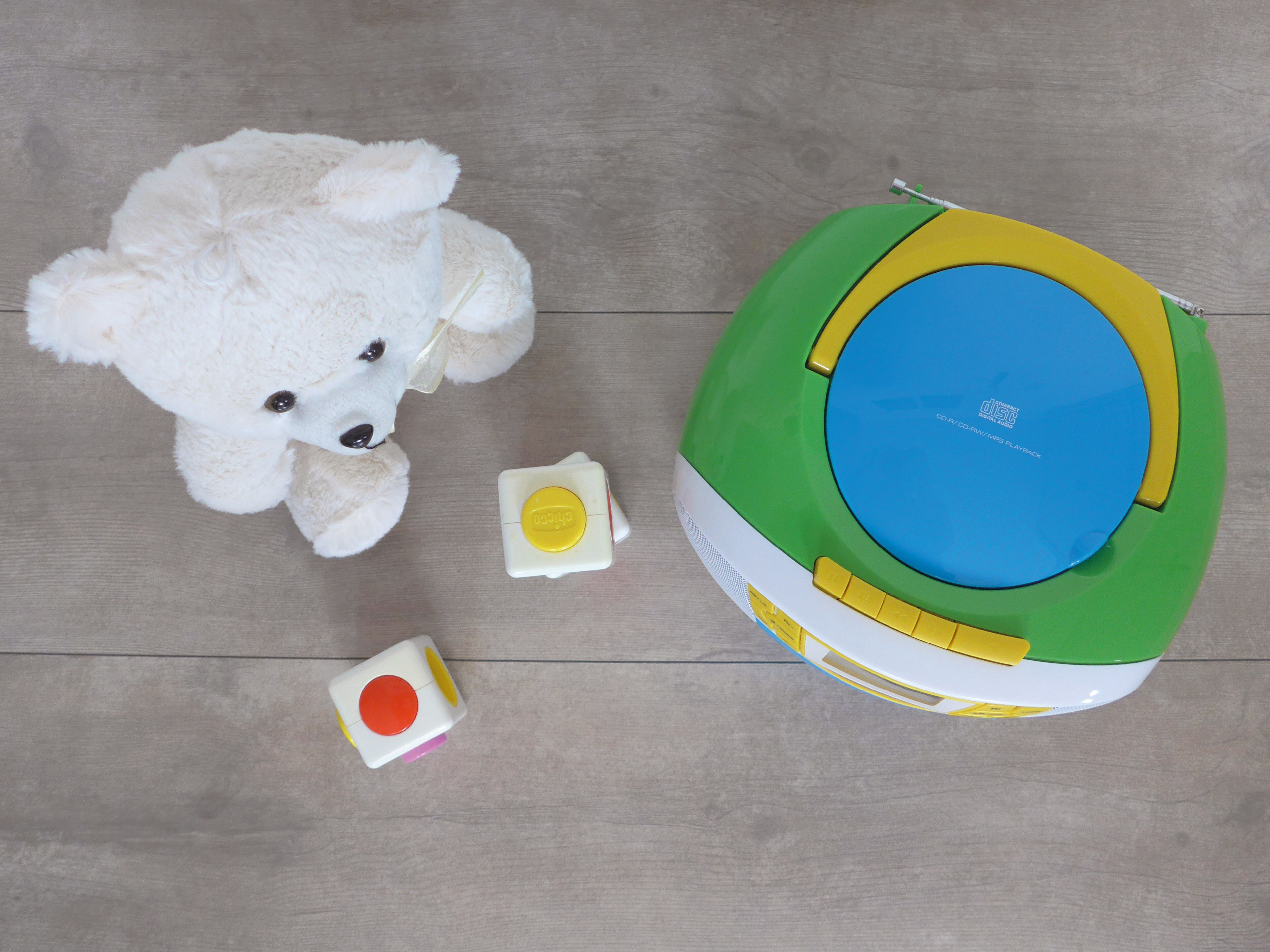 Draufsicht auf einen Teddybär, einen CD-Player und bunte Würfel. Holzoberfläche.