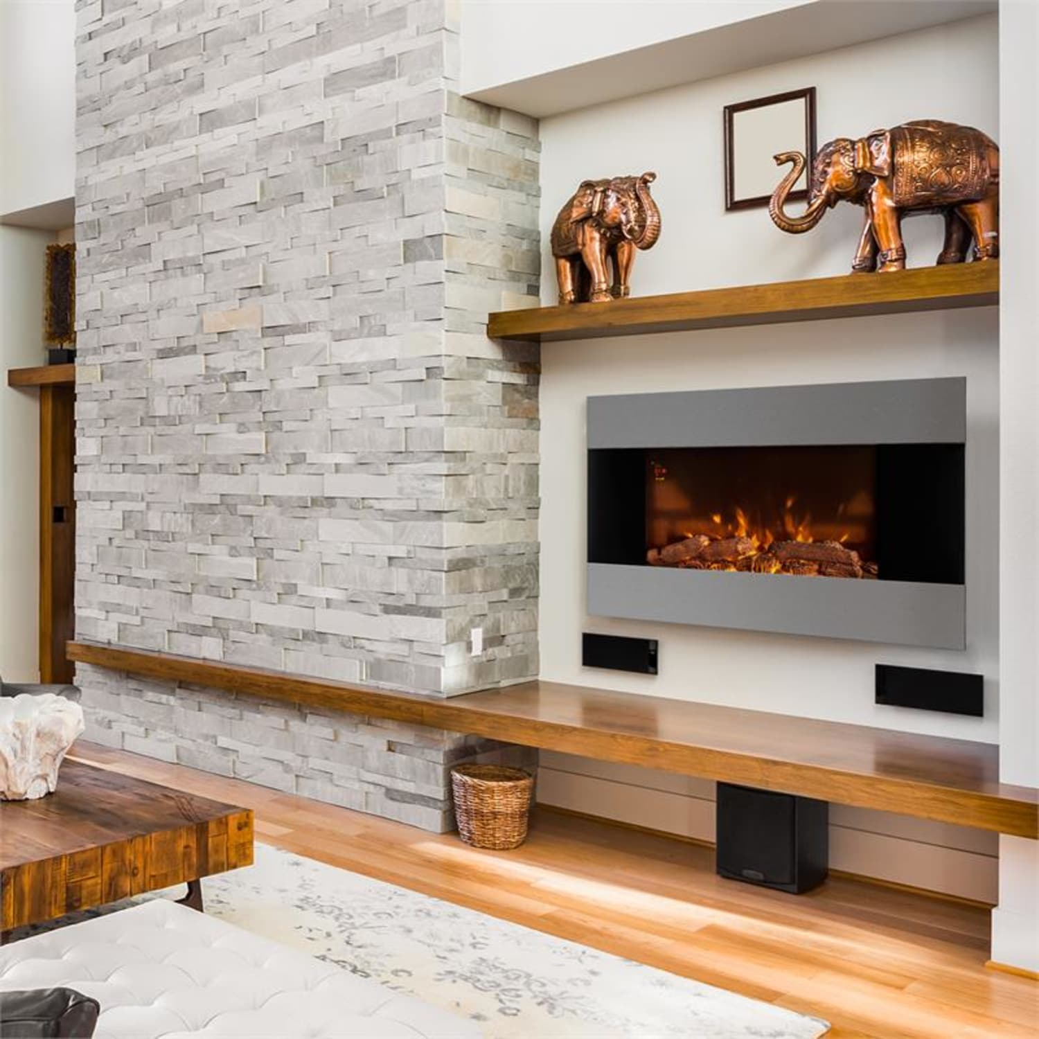 Kamin an einer Wand mit Steintextur. Es gibt dekorative Elefanten und ein Holzregal.