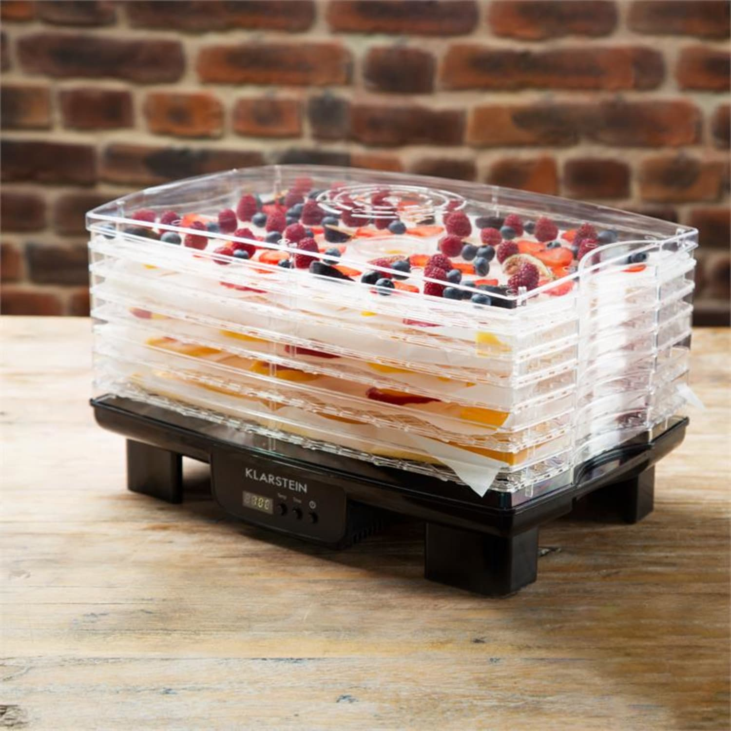 Lebensmitteltrockner mit transparenten Tabletts, gefüllt mit Obst, auf Holzoberfläche.