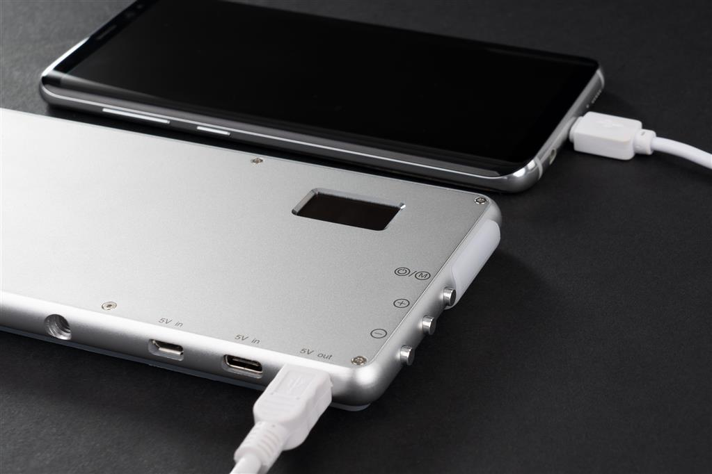 Silberne Powerbank, die ein schwarzes Smartphone mit weißem Kabel lädt.