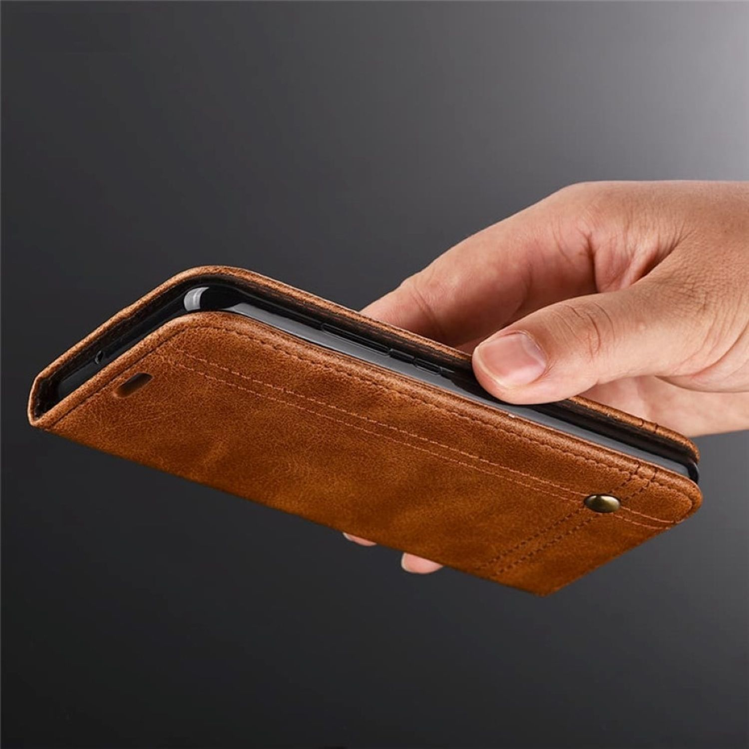 Hand, die eine offene, braune Leder-Handyhülle hält, die ein schwarzes Telefon zeigt.