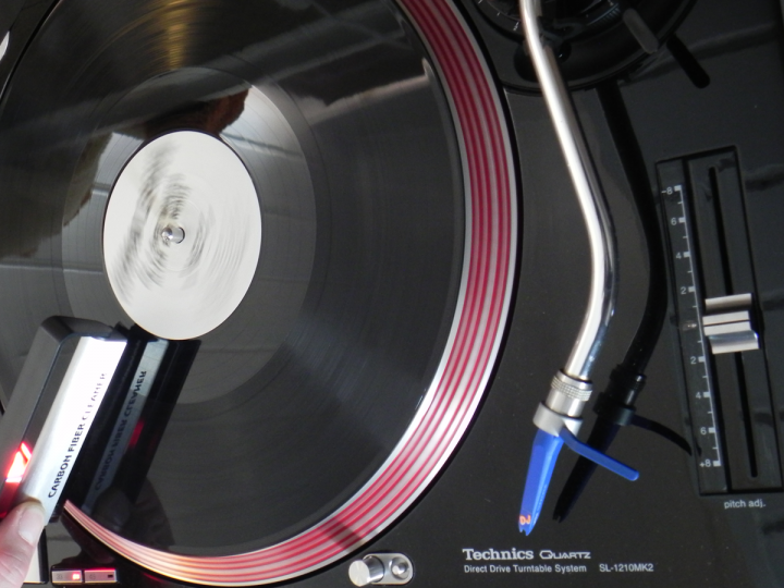 Plattenspieler mit Vinyl-Schallplatte. Ein Plattenreiniger berührt die Platte. Ein Tonabnehmer ist nah.