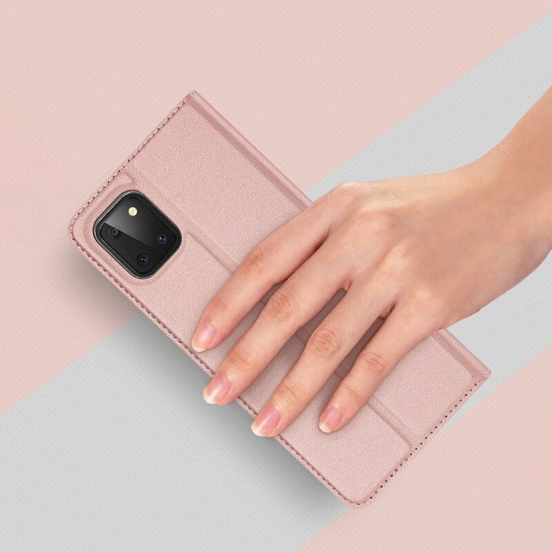 Eine Hand, die eine rosa Handyhülle mit Kameraausschnitt hält. Rosa und heller Hintergrund.