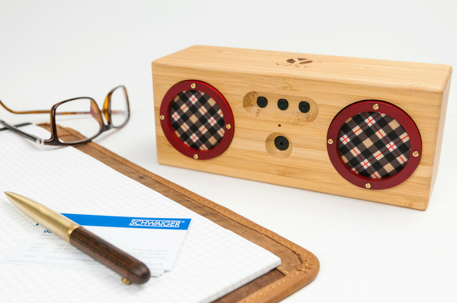 Holz-Lautsprecher mit roten Akzenten, Brille, Stift und Notizblock.