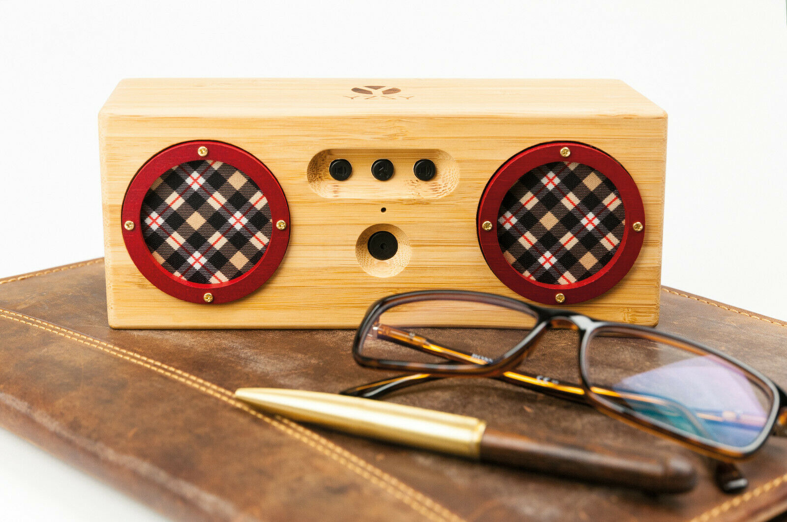 Holzlautsprecher mit roten Gittern und einer braunen lederartigen Oberfläche. Brille und Stift liegen oben.