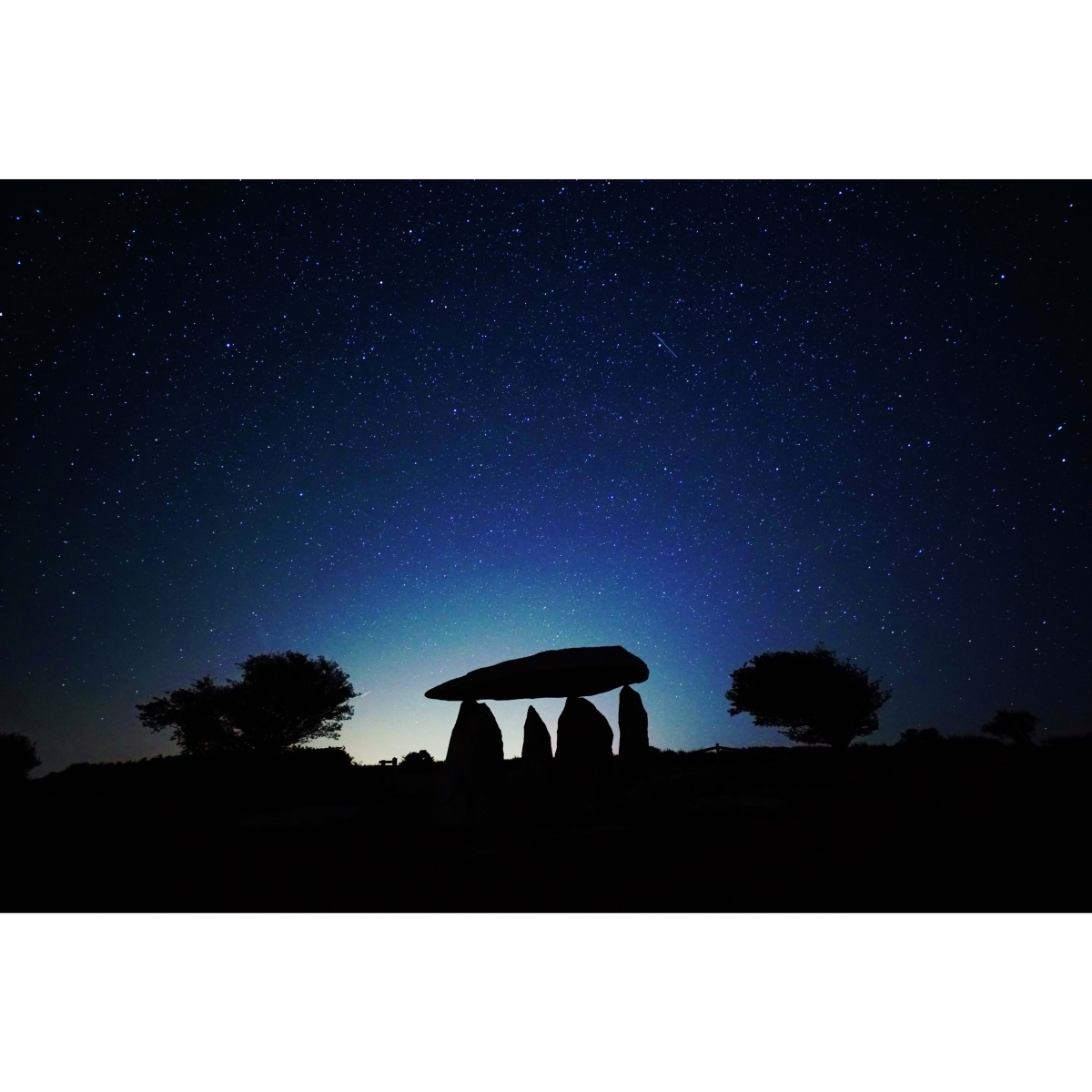 Nachthimmel mit Sternen über einer Silhouette aus Stein und Bäumen.