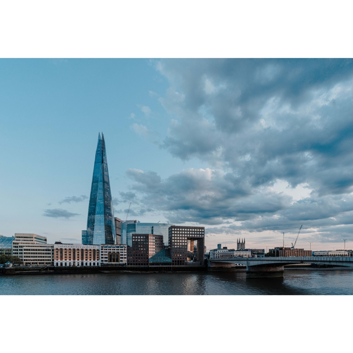 Stadtlandschaft mit The Shard im Hintergrund. Eine Brücke überspannt den Fluss mit Gebäuden im Vordergrund.