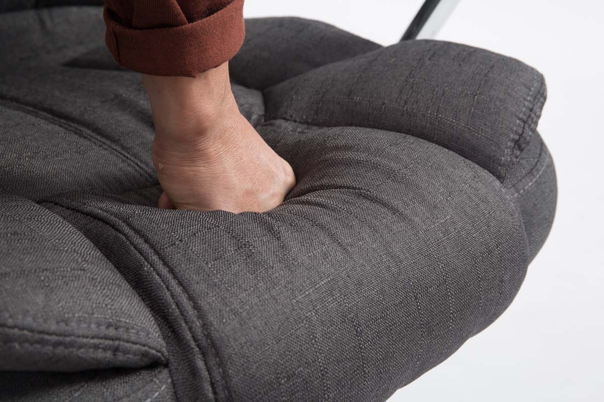 Hand drückt in eine graue, gepolsterte Oberfläche.