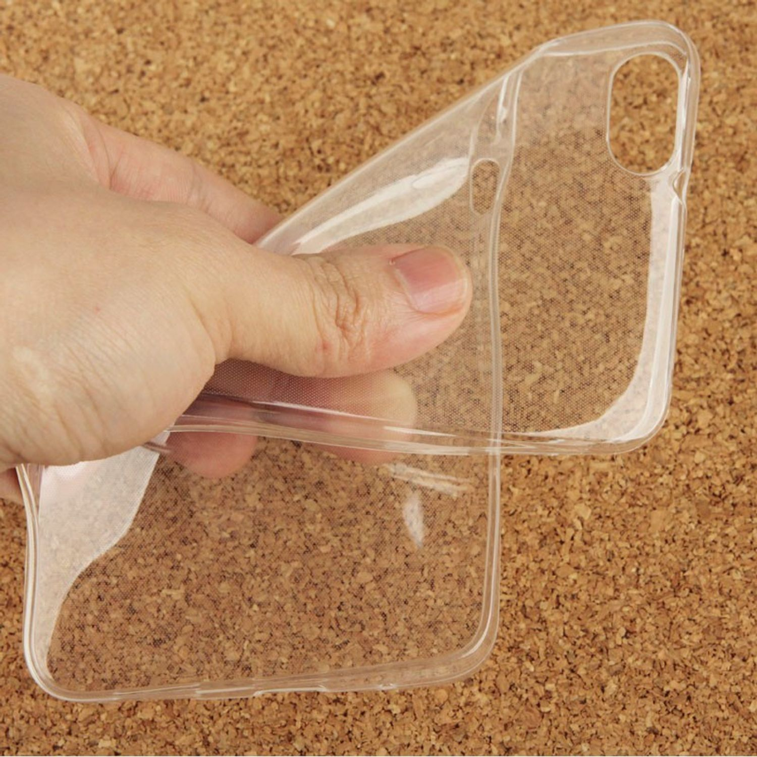 Hand hält eine klare, transparente Handyhülle. Korkhintergrund.