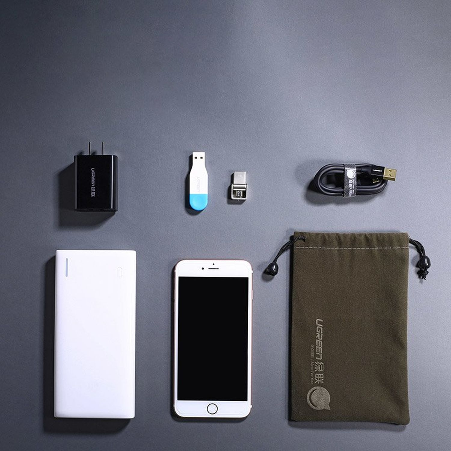 Assortimento di accessori tecnologici: caricabatterie, chiavetta USB, cavo, power bank e telefono. Sfondo grigio.