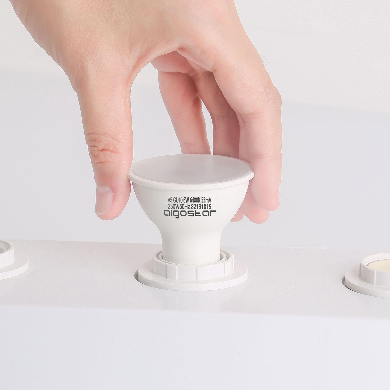 Una mano inserisce una lampadina bianca in un portalampada bianco.