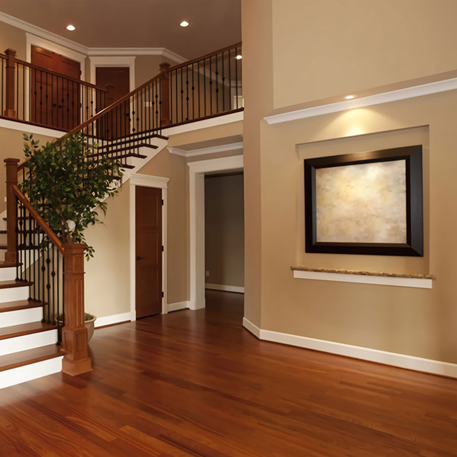 Un grande interno con scala in legno, pianta in vaso e quadro incorniciato su muro beige.