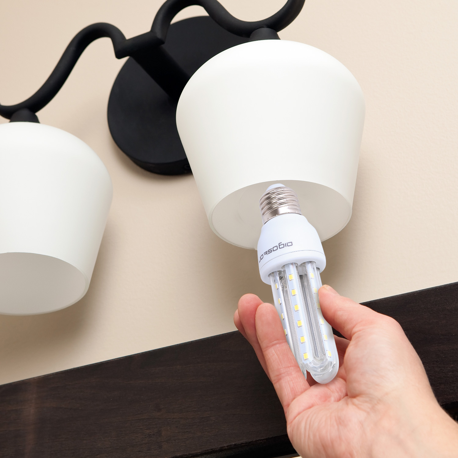 Mano che installa una nuova lampadina LED in un paralume bianco, sopra una trave marrone scuro.